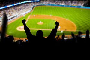 Fans raise their hands in excitement at a baseball game.